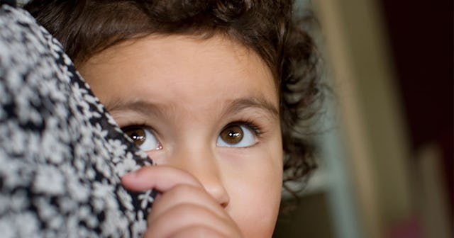 A closeup of a frightened child hiding her face behind her mom's dress who is not forced to hug othe...