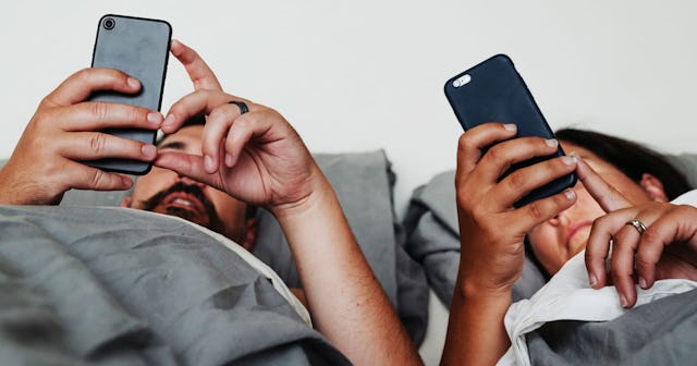 Two people in relationship on their smartphones while being together in bed