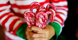A kid wearing a red-and-white striped sweater holding a bunch of candy canes