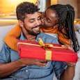 A woman handing down her husband a meaningful holiday gift wrapped in red decorative paper.