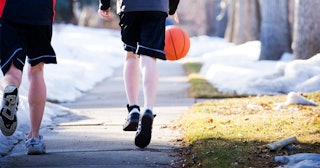 Two boys playing basketball, wearing shorts, while there is snow around them