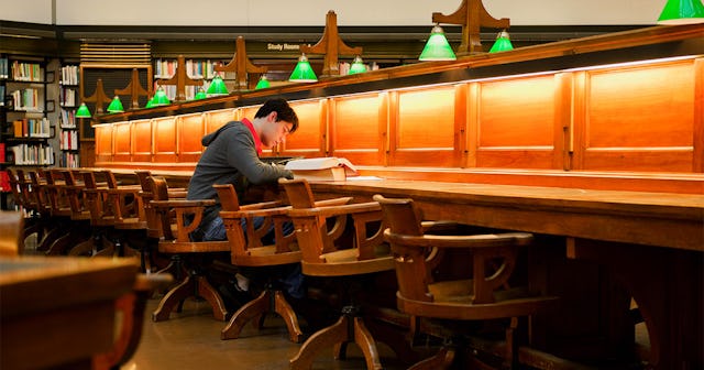 An anxious teenage boy sitting in a library alone and reading a book, while seeking perfect grades