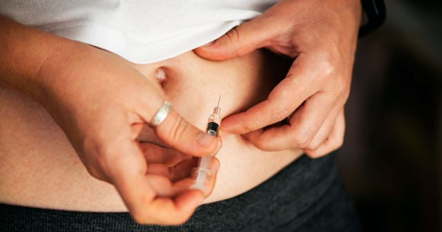 A woman receiving IVF treatment administering an injection to her abdominal area.