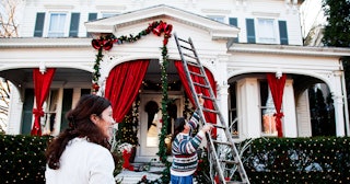 Family preparing a large white house for the winter holidays by decorating its exterior