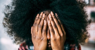 A young woman with curly hair holding hands on her face while being stressed 