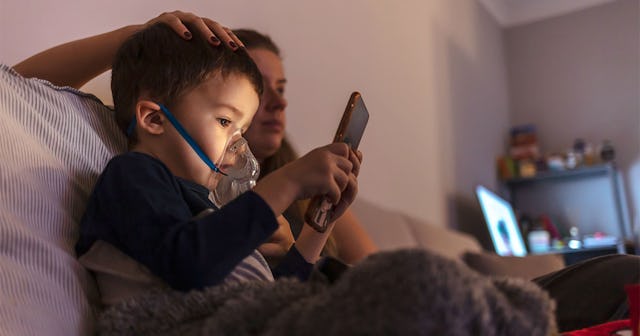A little boy with asthma playing games next to his father while sitting on a couch