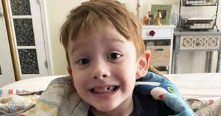 An autistic boy with brown hair and a blue shirt smiling at the camera in his room