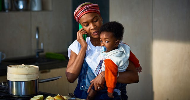 A mother talking on a mobile phone while holding her child with pacifier in his mouth