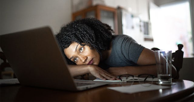 A curly-haired woman leaning on her laptop while looking at the screen