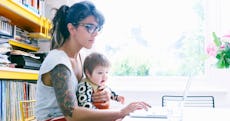 A single mom works on her computer as her toddler looks on.