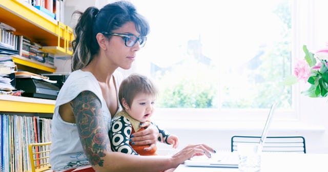 A single mom works on her computer as her toddler looks on.