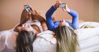 Two teen friends lying on a bed and using their phones 