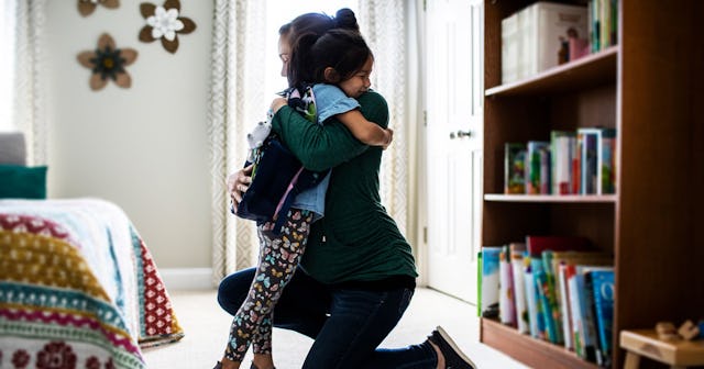A mom crouching down and hugging her child in the bedroom