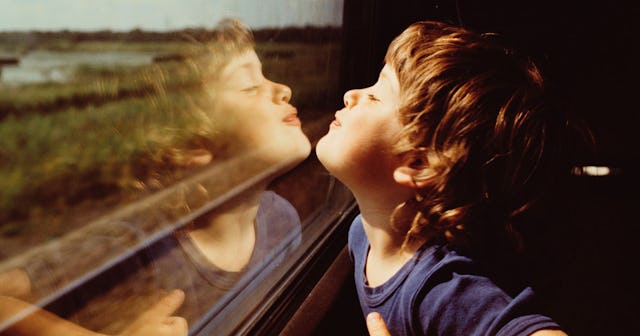 A toddler in a blue t-shirt looking at its reflection on a window in a train