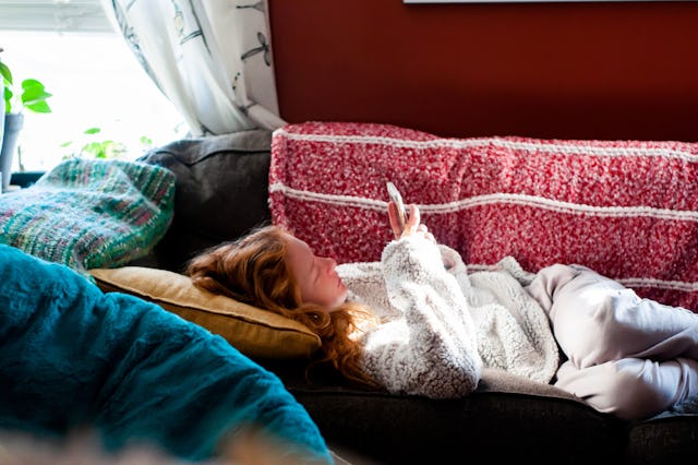Teenage girl laying on a red sofa texting, dealing with heartbreak
