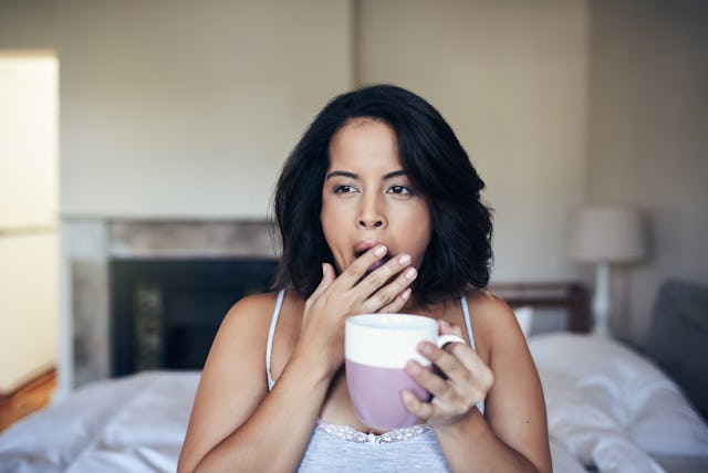 Image of a woman at home yawning over morning coffee