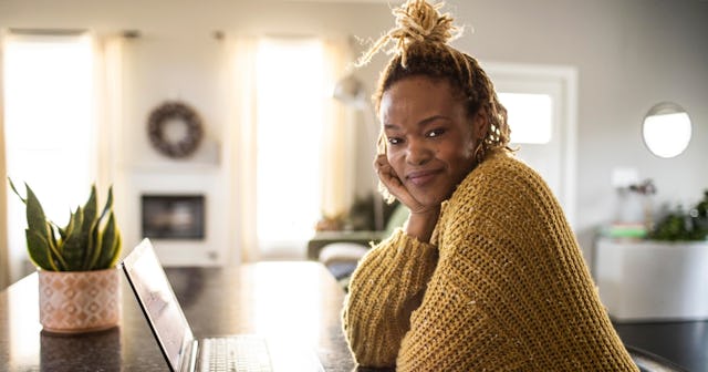 A confident woman sits in front of her computer, smiling.