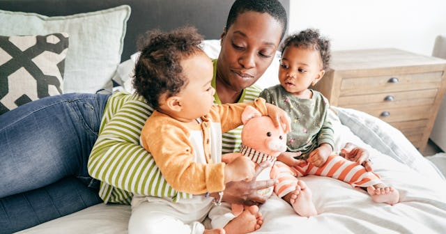 A mother plays on the bed with her two babies.