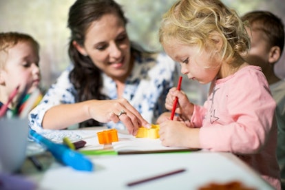 A daycare teacher helps kids with arts and crafts.