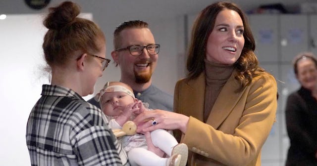 A woman holding a baby and Kate Middleton holding the baby's hand and smiling