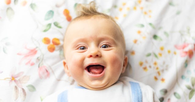 A happy, smiling baby lays in a crib.