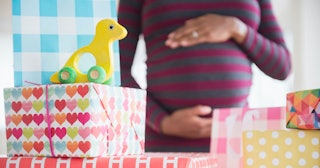 A pregnant woman holding her belly with presents for her baby shower in front of her.