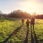 A mother and her two young sons walking in a country park in low winter sunlight, with their long sh...