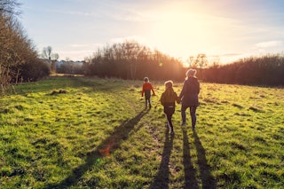 A mother and her two young sons walking in a country park in low winter sunlight, with their long sh...
