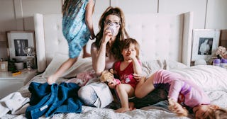 A mom drinking coffee and trying to relax in her bed with her three children playing and jumping on ...