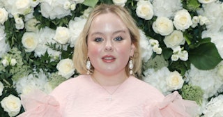 Nicola Coughlan in a pink dress standing in front of a wall of white roses.