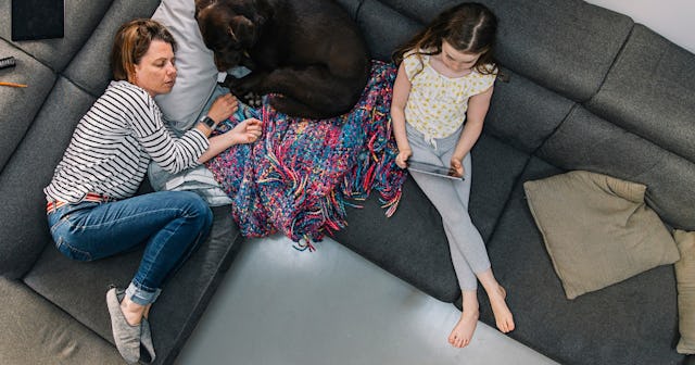 A tired mom sleeps on the couch with her tween and dog.