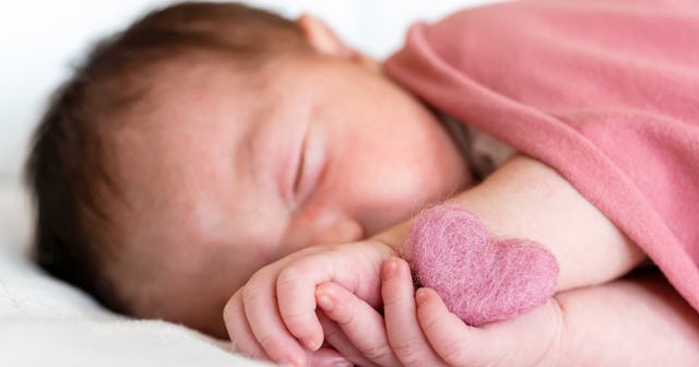 A swaddled baby snuggles with a felt heart.