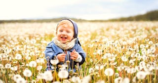 A baby sits in a field of dandelions.