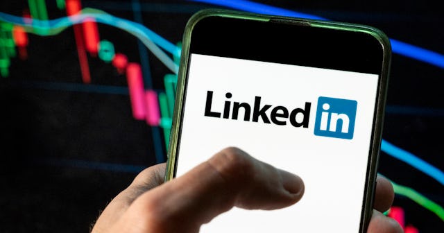 A hand is holding a mobile phone with the LinkedIn logo on the screen.