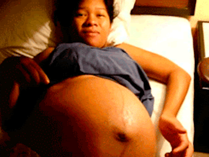 Gif of a pregnant black woman wearing a gray shirt with her belly out and an unborn baby moving in i...