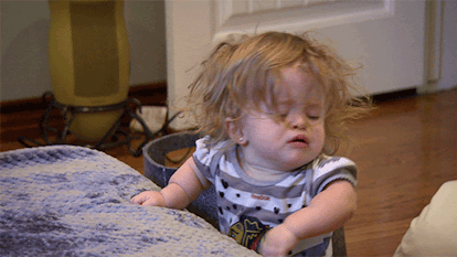 A GIF of a crying toddler leaning on the edge of a bed