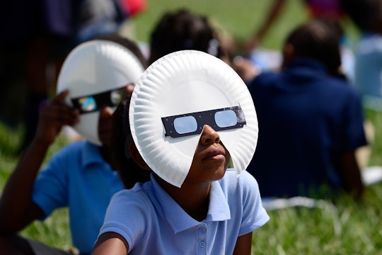 Little kids in a park with paper plates and sunglasses on their faces to watch the Solar Eclipse saf...