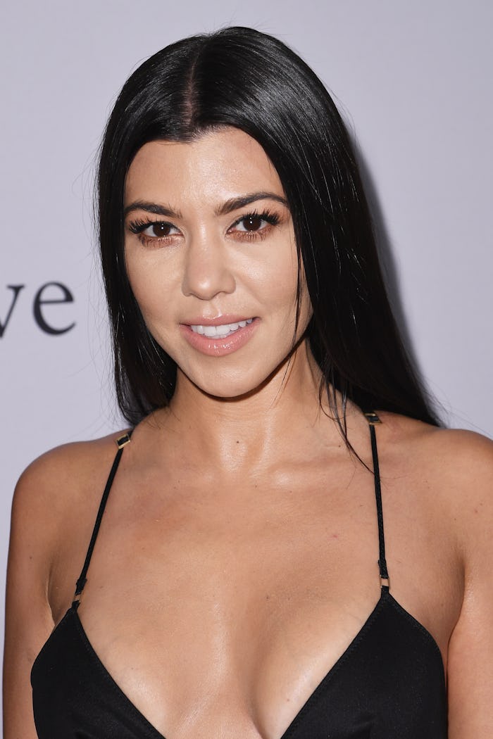 Kourtney Kardashian in a black strappy dress with her hair down, posing at a red carpet