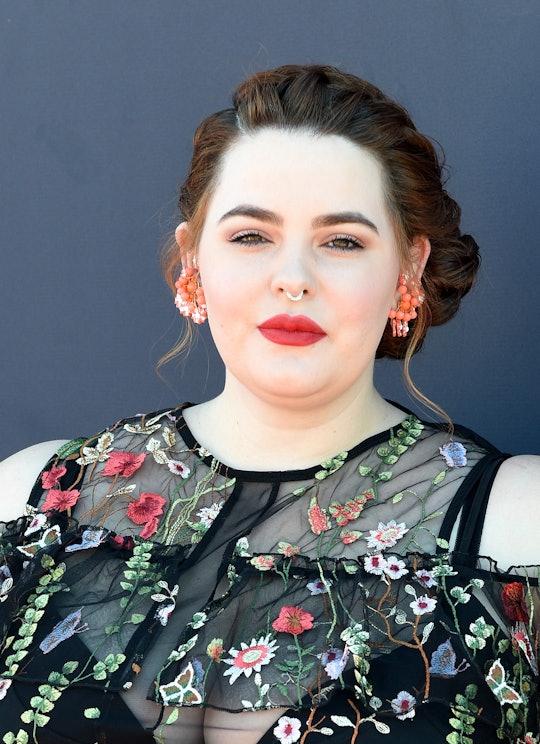 Tess Holliday posing in a sheer black dress with a floral pattern at a red carpet event.