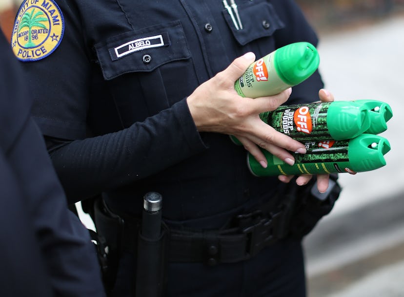 Miami police officer holding four mosquito repellent sprays.