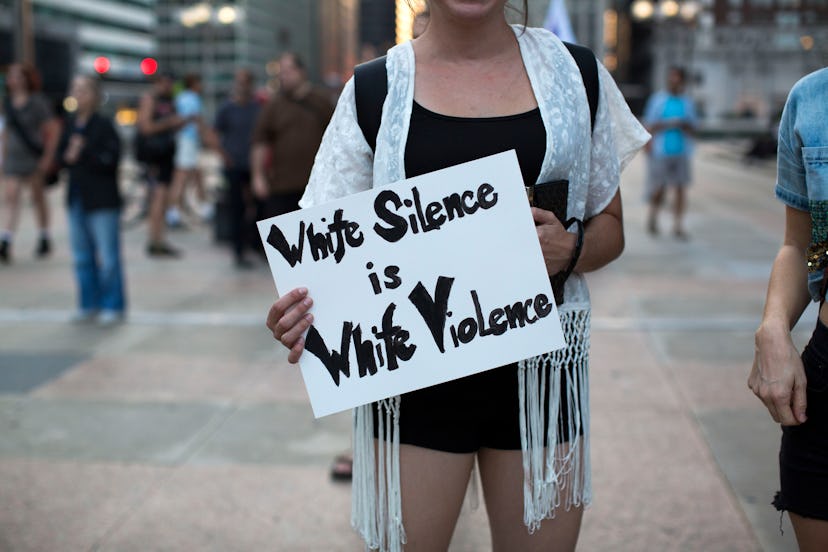 A woman holding a poster with "white silence is white violence" text