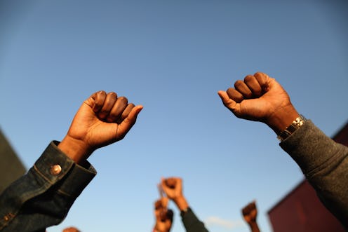 A Black woman holds two fists up. These quotes from Black leaders can be excellent Black History Mon...