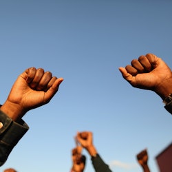 A Black woman holds two fists up. These quotes from Black leaders can be excellent Black History Mon...