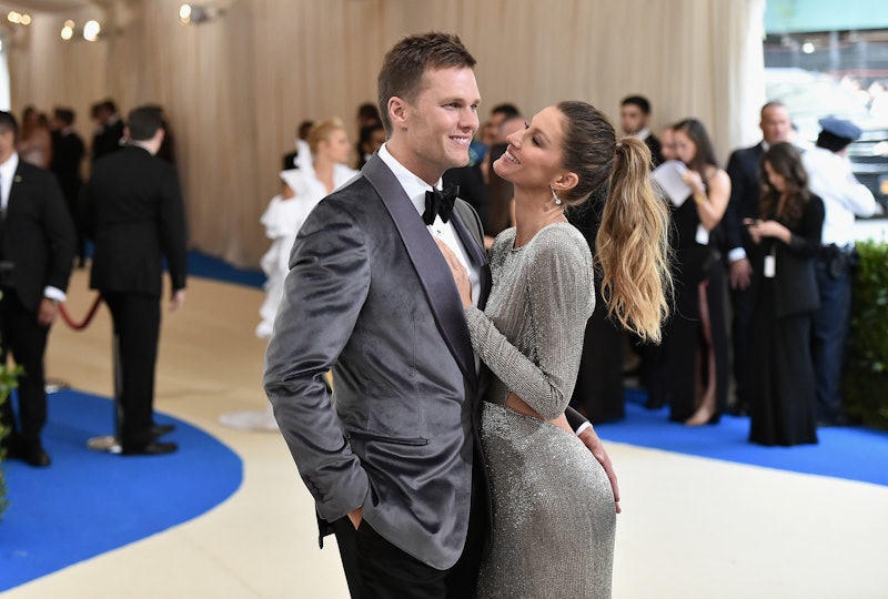 Tom Brady in a grey suit and black bowtie hugging Gisele Bündchen in a long shiny grey dress with an...
