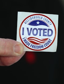 A mans hand holding a sticker that says ‘I voted’.