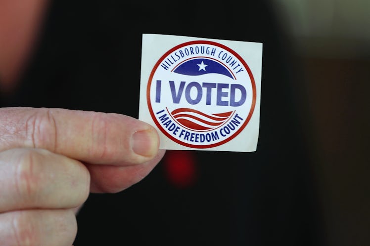 A mans hand holding a sticker that says ‘I voted’.