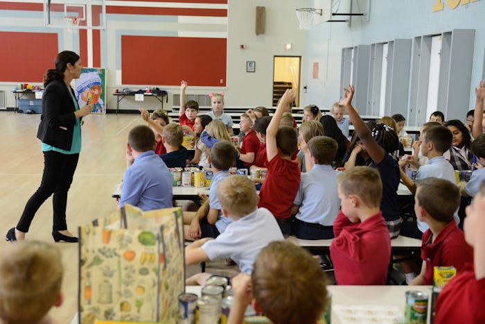 A mom volunteering in her child's classroom at the gym, as multiple kids raise their hands