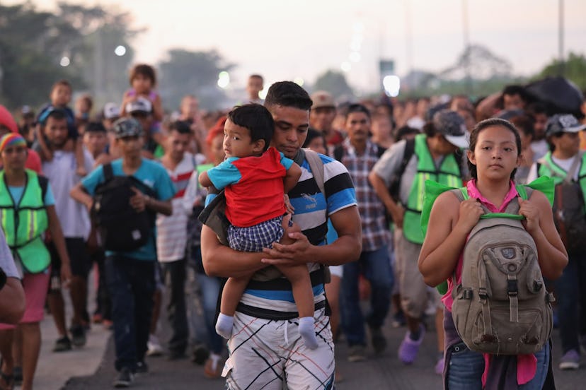 A group of Migrant Caravan Families & Children walking down the street, in focus a man carrying a ch...