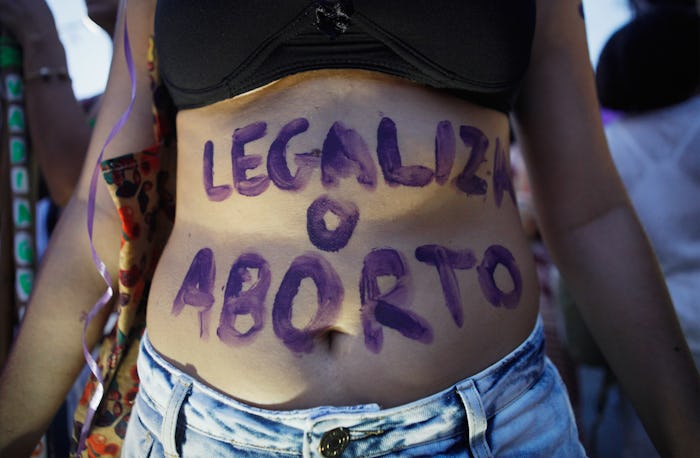 A woman posing with a "legaliza o aborto" blue tempera paint text on her belly