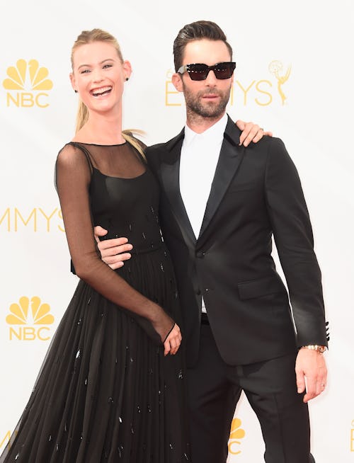 Adam Levine in a suit and sunglasses & Behati Prinsloo in a black dress posing on a red carpet 